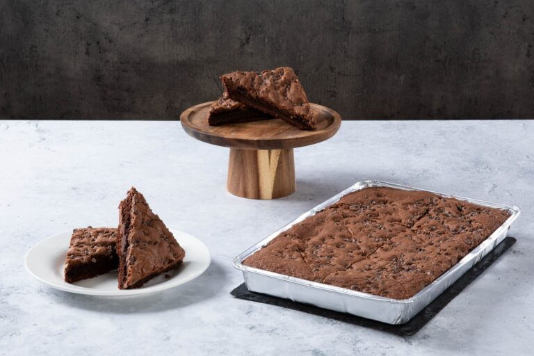 Chocolate brownie traybake with chocolate chips, served sliced and in a baking tray.