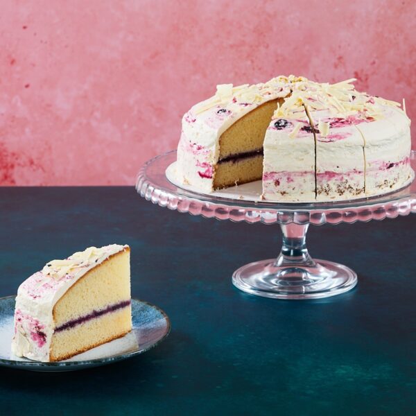 Lemon and blueberry cake with white chocolate topping on a glass cake stand.